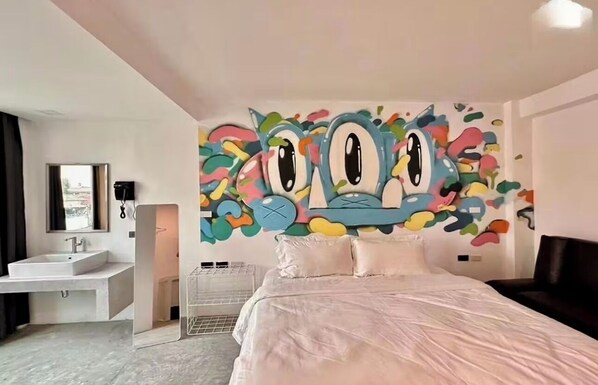 Moderni hotellihuone, jossa on suuri sänky, valkoinen kylpyhuone ja värikäs seinämaalaus.