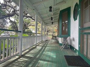 A covered porch with a wooden floor, white railings, and green trim.