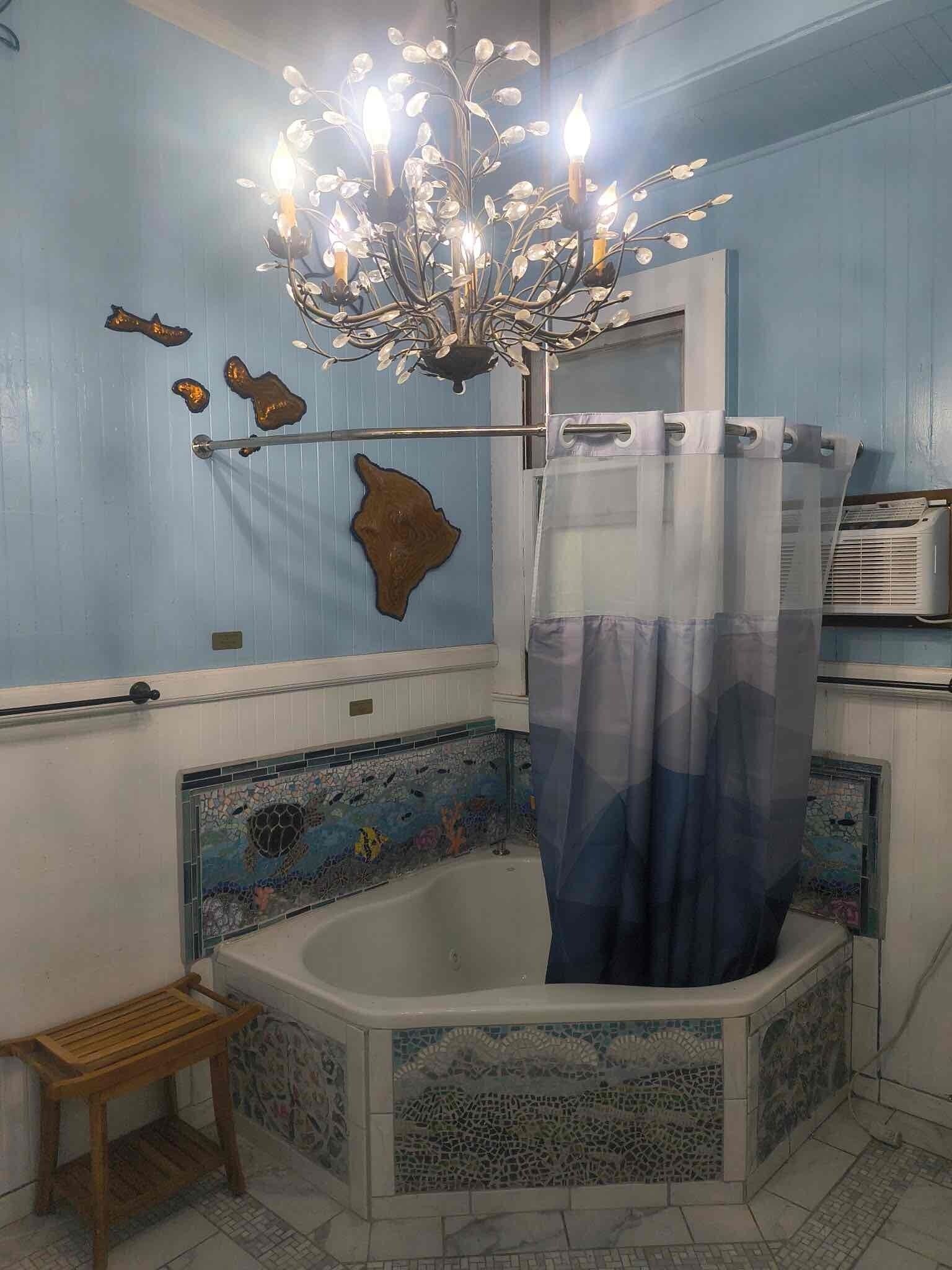Une salle de bain avec une baignoire, un rideau de douche, un tabouret en bois et un lustre décoratif.