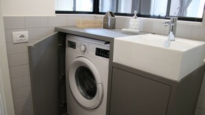 Ein kleiner Waschbereich mit Waschmaschine, Spüle und einem fenster mit Vorhängen.