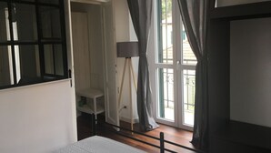 Ein Zimmer mit Bett, Schreibtisch, Lampe und einem Fenster mit Vorhängen.