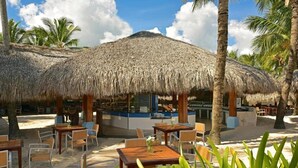 A beachside restaurant with thatched umbrellas, outdoor seating, and palm trees. - Iberostar Waves Punta Cana (Punta Cana)