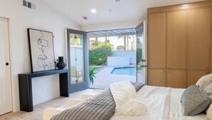A bedroom with a bed, a bedside table, a wardrobe, and a view of a swimming pool. - Playful Luxury - Pool, Games & Near Old Town (Scottsdale)