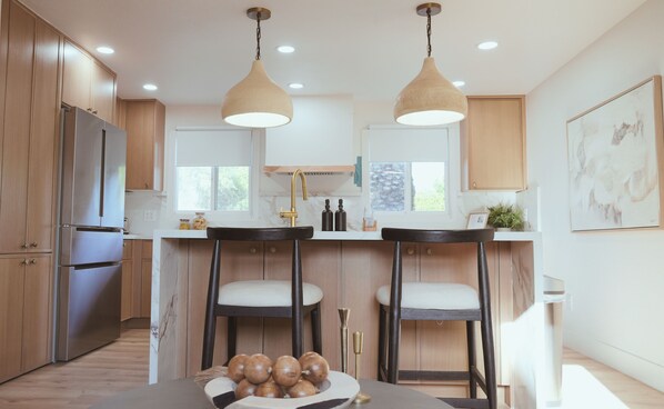 A modern kitchen with wooden cabinets, stainless steel appliances, pendant lighting, and a marble countertop. - Playful Luxury - Pool, Games & Near Old Town (Scottsdale)