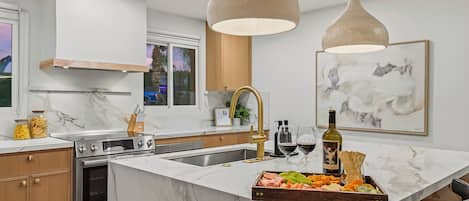 A modern kitchen with a marble island, stainless steel appliances, and pendant lighting.