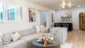 A modern living room with a sectional sofa, a round coffee table, and a dining area with a small table and chairs. - Playful Luxury - Pool, Games & Near Old Town (Scottsdale)