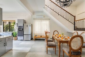 A modern kitchen with a dining area, a staircase, and a view of the outdoors. - Vagator Maison by Dia Hotels and Homes (Anjuna)