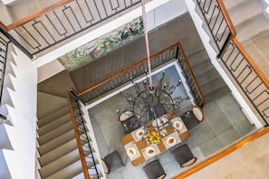 A multi-level interior with a dining area featuring a chandelier, a staircase, and a decorative ceiling.