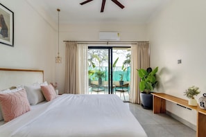 A bedroom with a bed, a bedside table, a potted plant, and a view of the outdoors.