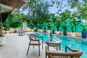 A pool area with wicker chairs and a glass table, surrounded by potted plants and a green wall. - Vagator Maison by Dia Hotels and Homes (Anjuna)