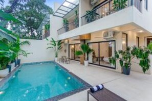 Un edificio moderno con piscina, mobiliario de exterior y plantas en macetas.