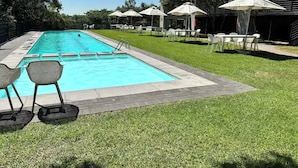 A swimming pool with a tiled deck, surrounded by grass and outdoor seating with umbrellas. - Dainfern Luxury Penthouse (Midrand)