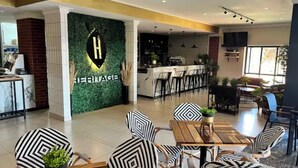 A modern hotel lobby with a reception desk, patterned chairs, and a dining area. - Dainfern Luxury Penthouse (Midrand)