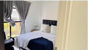 Ein Schlafzimmer mit Bett, Nachttisch, Blumenvase und Blick ins Freie.