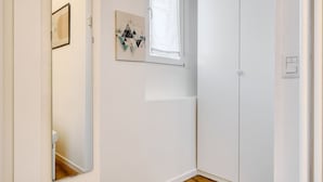 Une pièce avec une porte blanche, un miroir, une fenêtre et une œuvre d’art accrochée au mur.