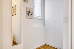 A room with a white door, a mirror, a window, and a wall-mounted artwork.
