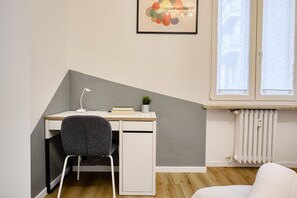 Un dormitorio en esquina con escritorio, silla, radiador y ventana.