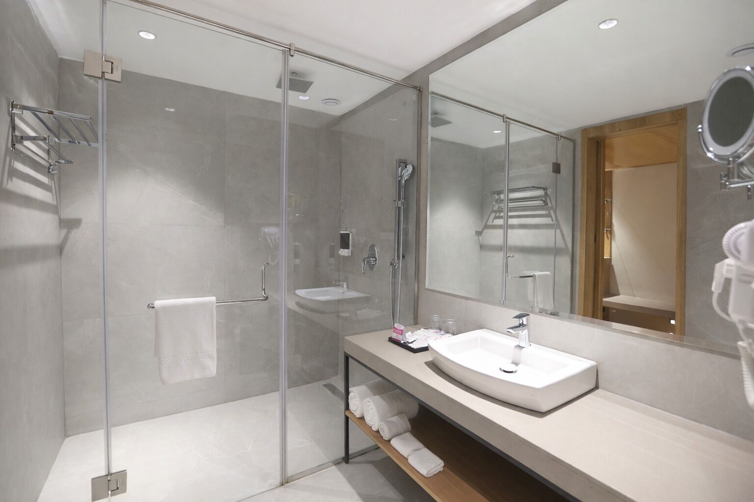Een moderne badkamer met een douchecabine van glas, een grote spiegel en een witte wasbak.
