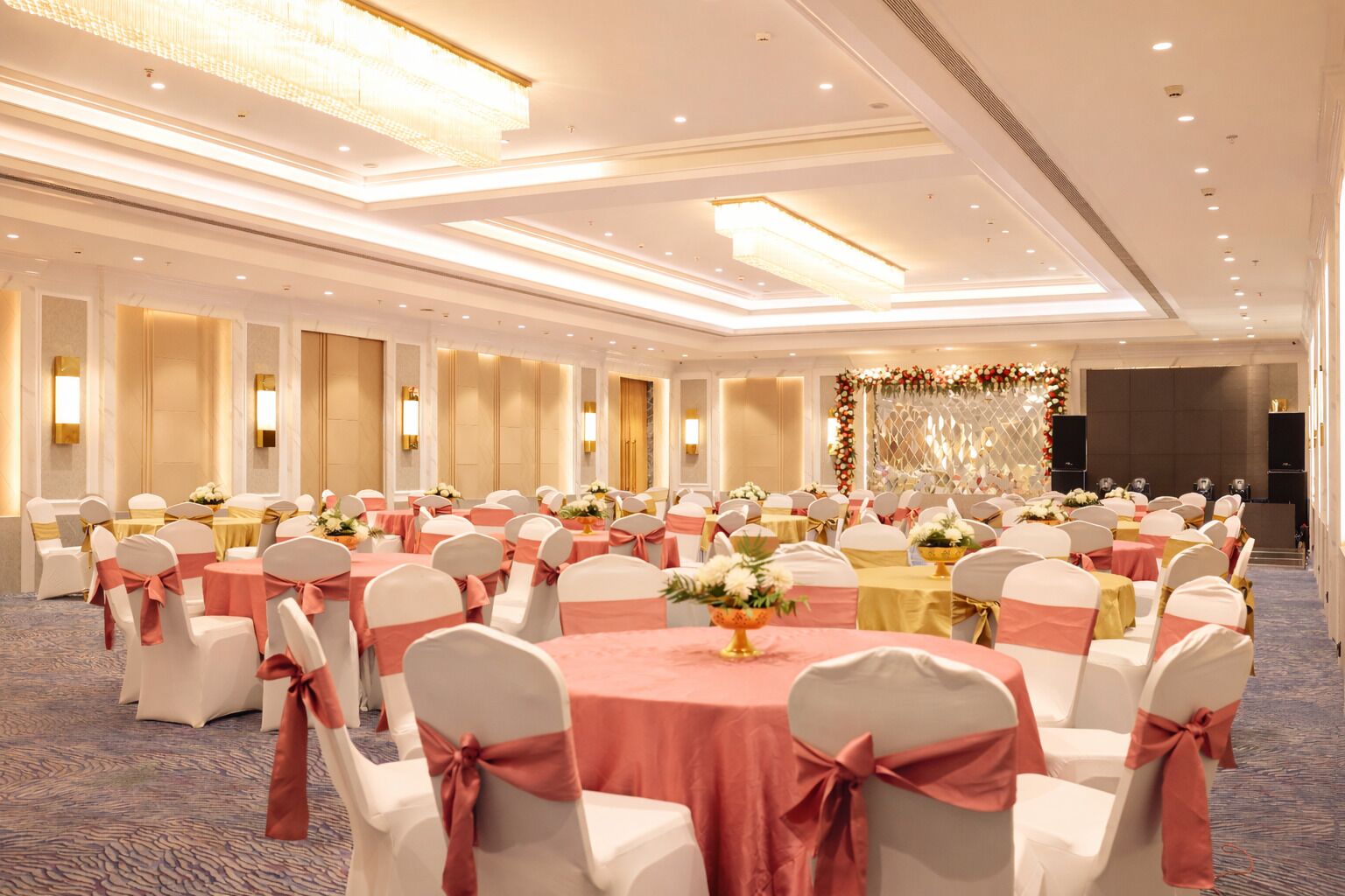 A large banquet hall with round tables, white chairs with pink sashes, and a decorative backdrop.