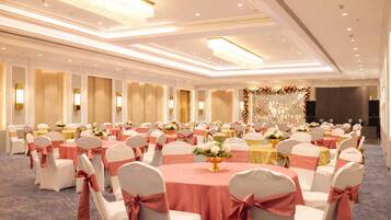 A large banquet hall with round tables, white chairs with pink sashes, and a decorative backdrop.