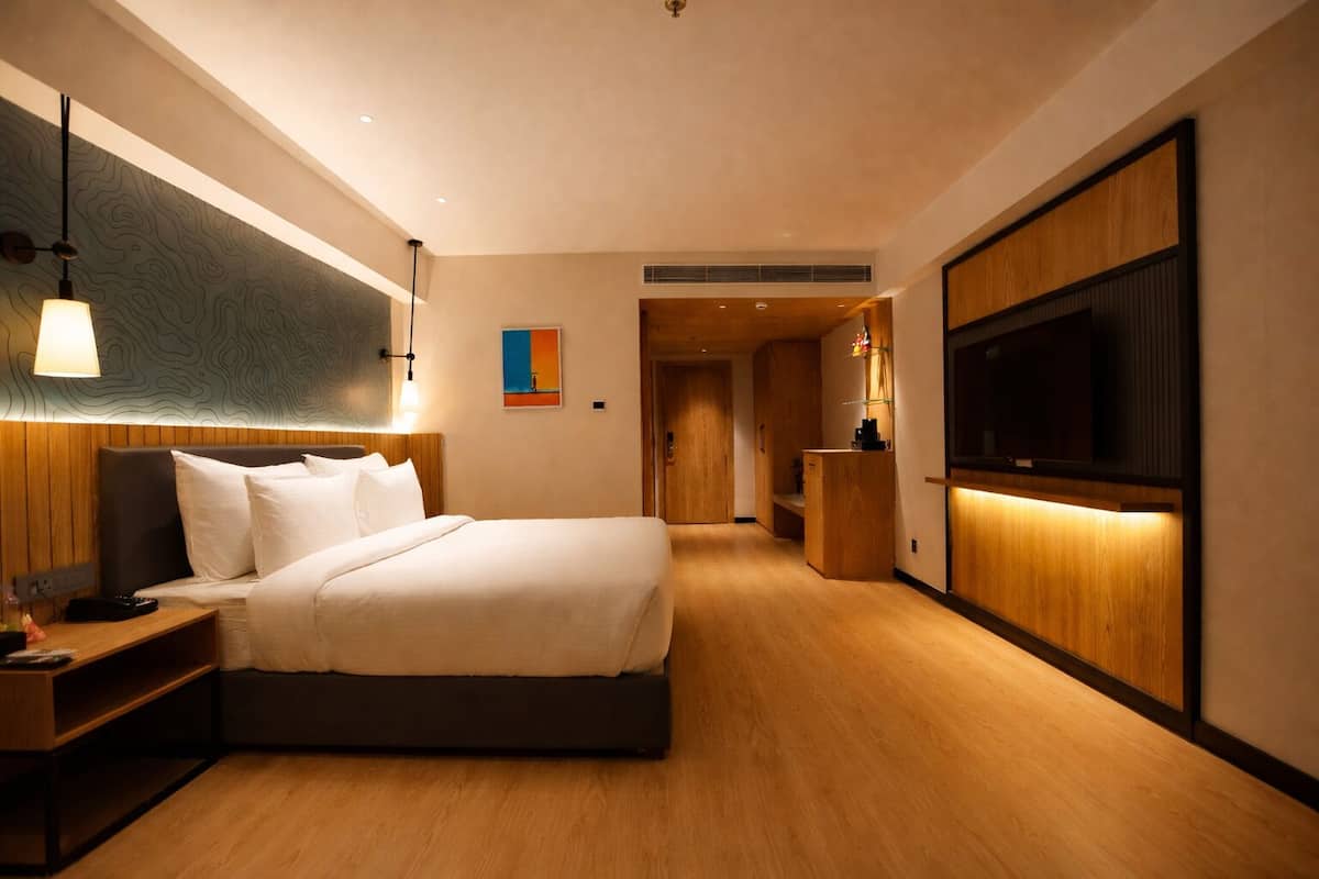 A modern hotel room with a large bed, bedside tables, a TV, and a wooden floor.