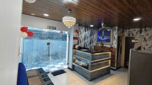 A reception area with a wooden ceiling, a chandelier, a reception desk labeled 'MocNLight,' and a wall-mounted TV. - Hotel Moon Light  (Indore)