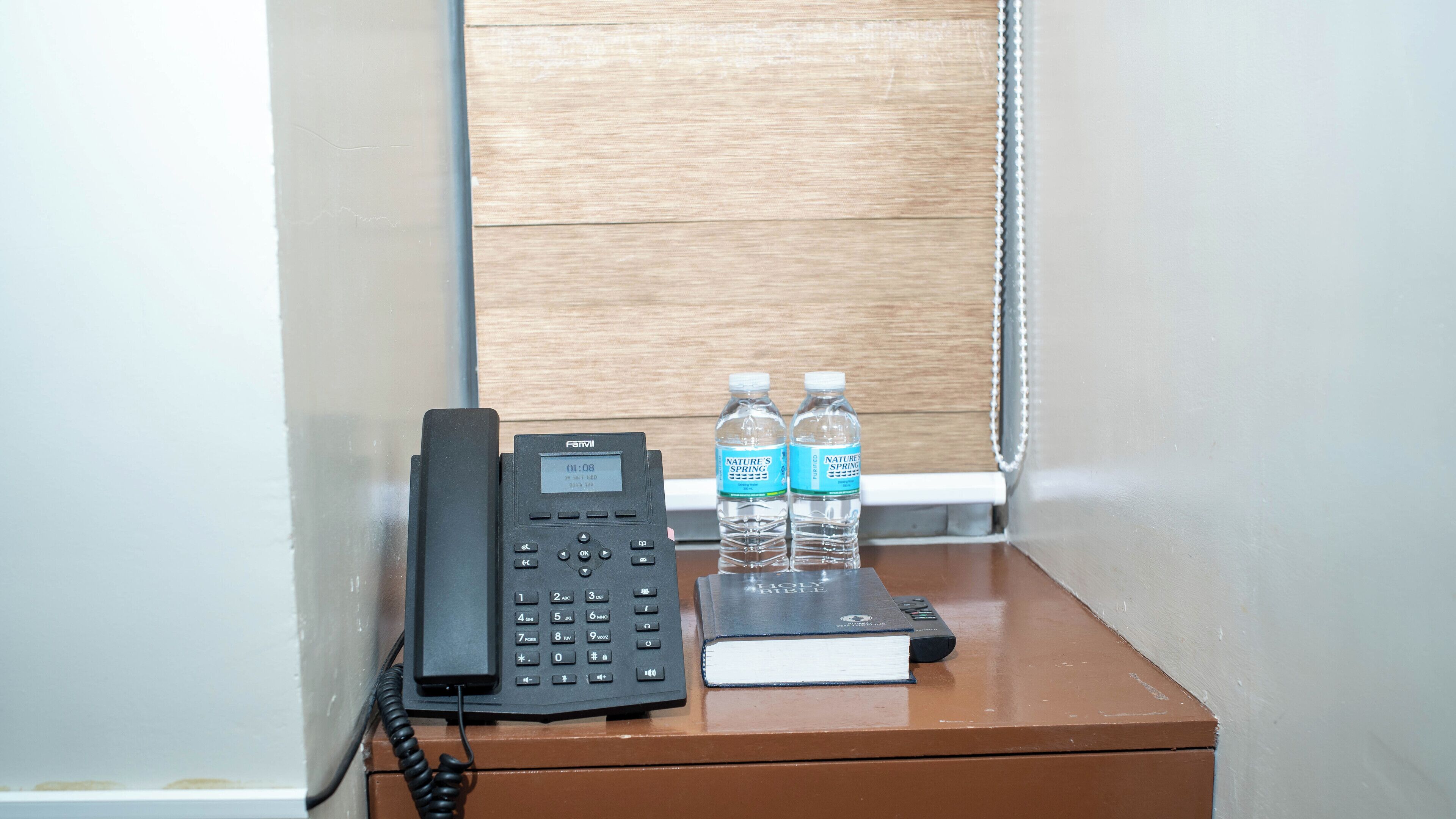 A hotel room with a telephone, two water bottles, and a book on a wooden table.