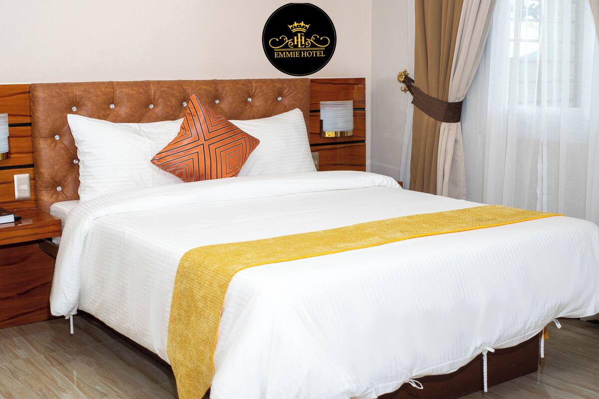 A hotel room with a wooden headboard, white bedding, a yellow throw, and a bed with two pillows.