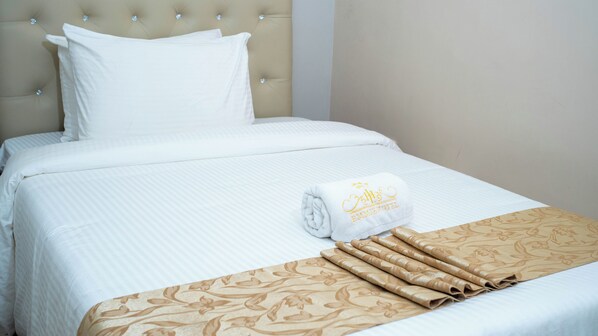 Una cama bien hecha con una toalla enrollada y una colcha estampada.