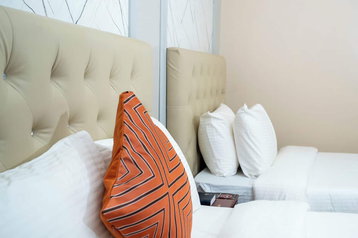 A hotel room with a tufted headboard, a bed with white bedding, and a striped pillow.