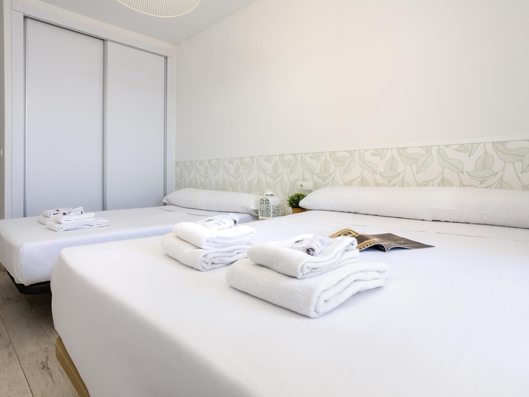 Ett hotellrum med två sängar, där varje säng har prydligt vikta, vita handdukar och en tidning liggande på sig.