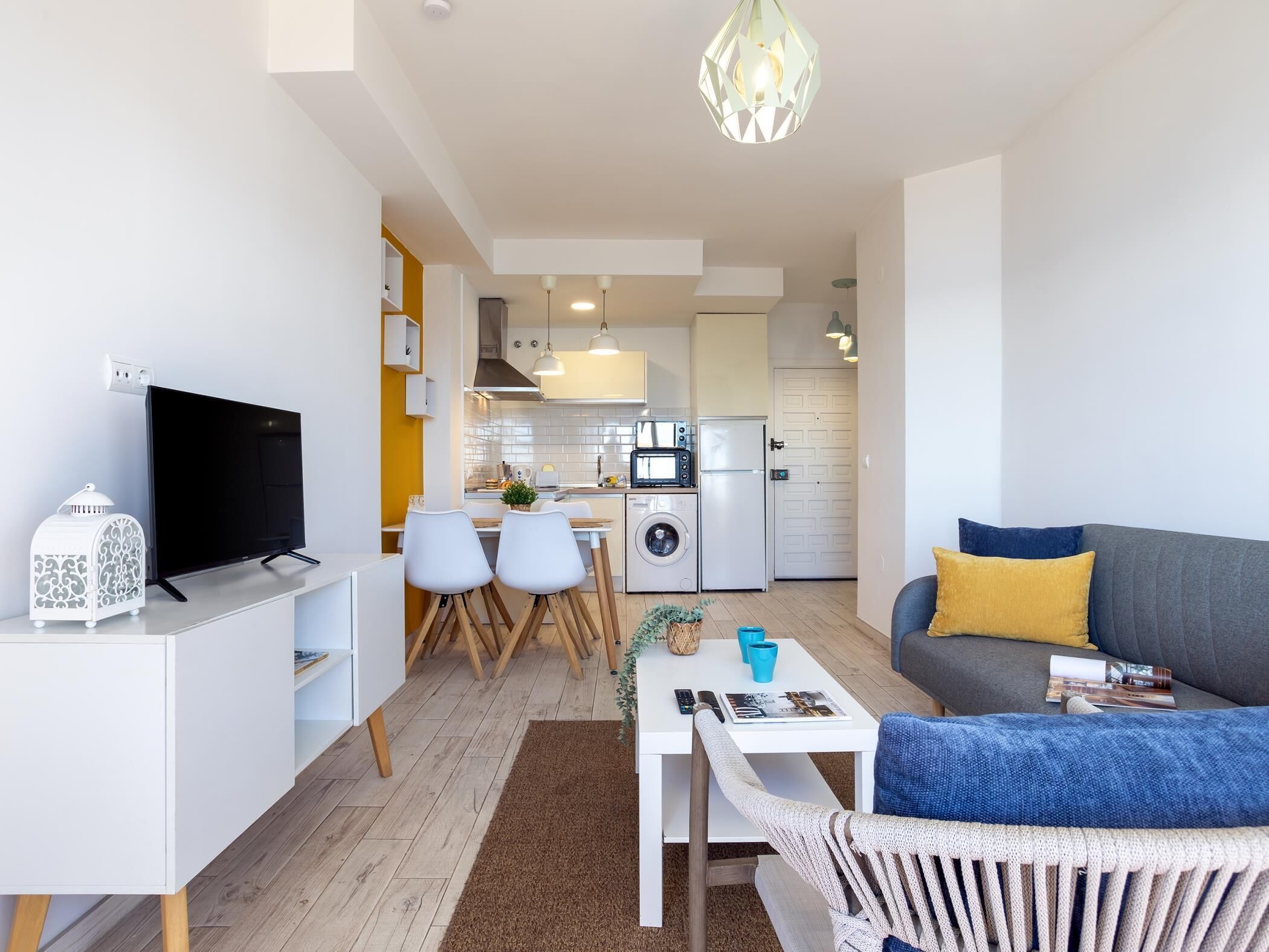 Un salon moderne doté d’un téléviseur à écran plat, d’un canapé avec des coussins, d’une table basse et d’un coin repas avec des chaises et une petite table.