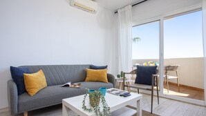 Una sala de estar moderna con un sofá gris, una mesa de centro blanca y un balcón con mesa y sillas.