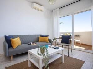 A modern living room with a grey sofa, a white coffee table, and a balcony with a table and chairs. - Sunstay Benalbeach Flat I Benalmadena (Benalmádena)