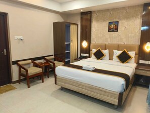 A hotel room with a bed, a desk, a chair, a wardrobe, and a wall-mounted light fixture. - Sri Ram Residency (Palayankottai)