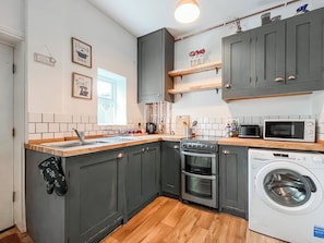 A compact kitchen with dark cabinets, a wooden countertop, a built-in oven, a microwave, and a washing machine. - 5 bedroom accommodation in Hinderwell, near Staithes (Hinderwell, near Staithes)