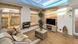 Amplia sala de estar con televisor grande, piso de madera, un sofá y un tragaluz.