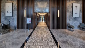 A modern hotel lobby with a geometric patterned carpet, marble flooring, and contemporary wall art. - Arlo By SanLiving - 2BR - HubLife Mall (Jakarta)