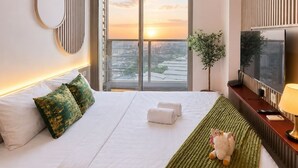 A modern hotel room with a large bed, a flat-screen TV, a balcony with a city view, and a decorative wall panel. - Arlo By SanLiving - 2BR - HubLife Mall (Jakarta)