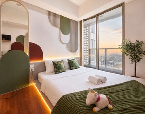 A modern hotel room with a large bed, a view of the city, and a green plant. - Arlo By SanLiving - 2BR - HubLife Mall (Jakarta)