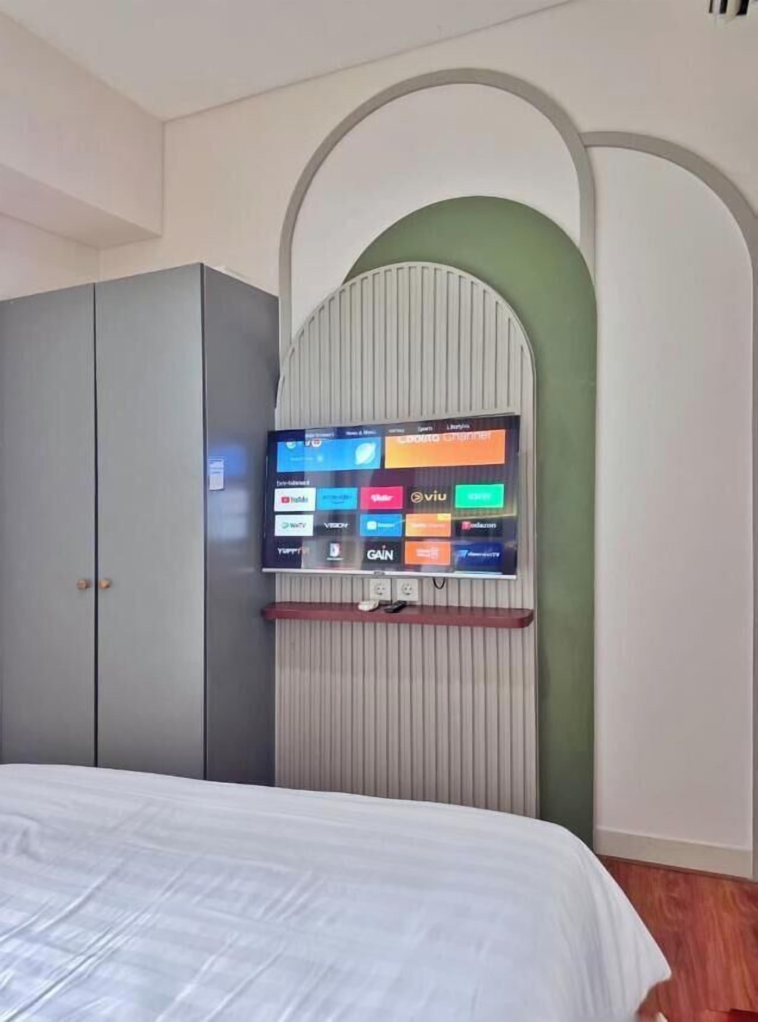 Ein Schlafzimmer mit einem Bett, einem grauen Kleiderschrank und einem an der Wand befestigten Fernseher, der verschiedene Streaming-Dienste anzeigt.
