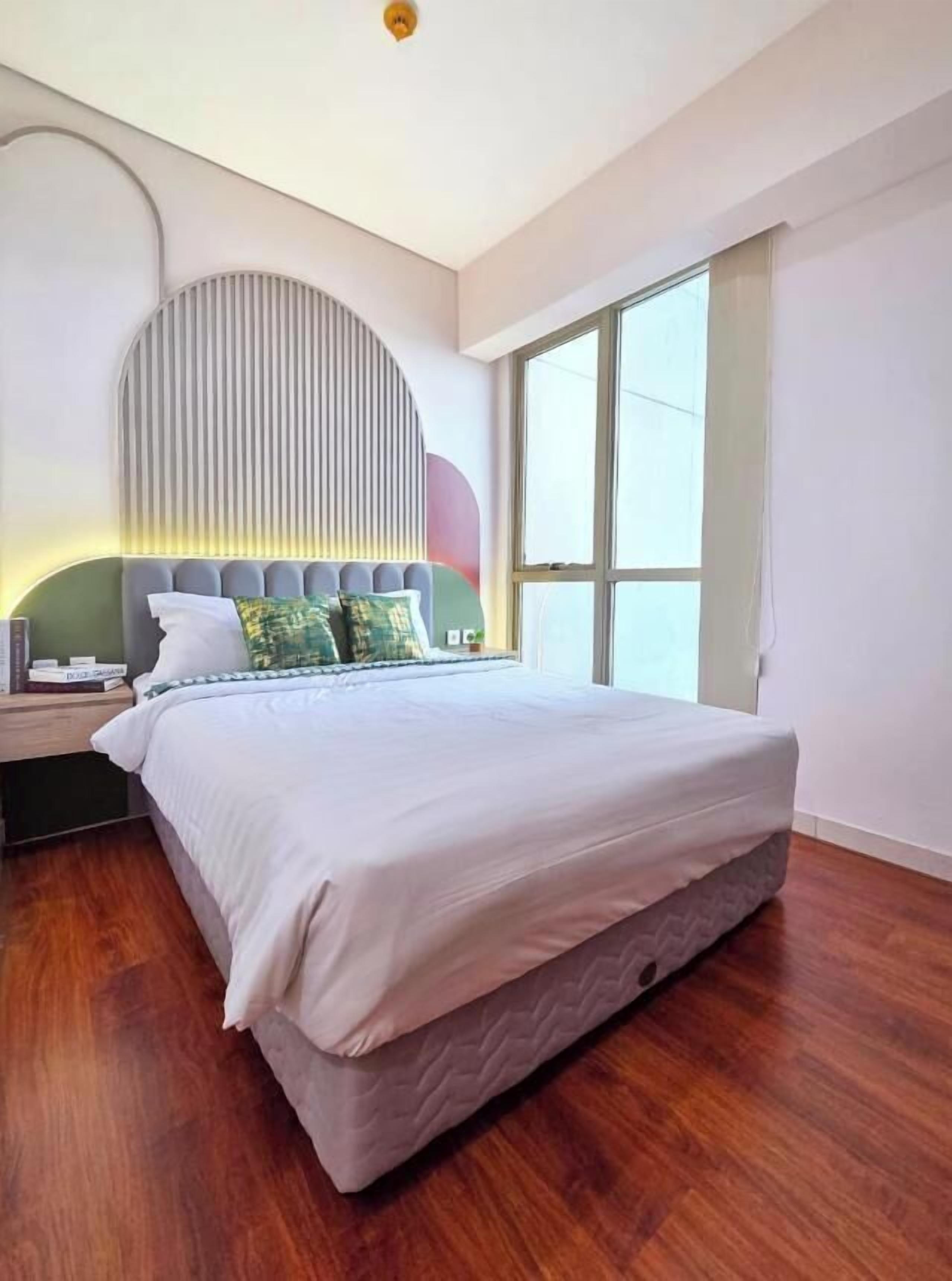 Un dormitorio moderno con una cama grande, una mesita de noche, una lámpara de pared y un ventanal amplio.