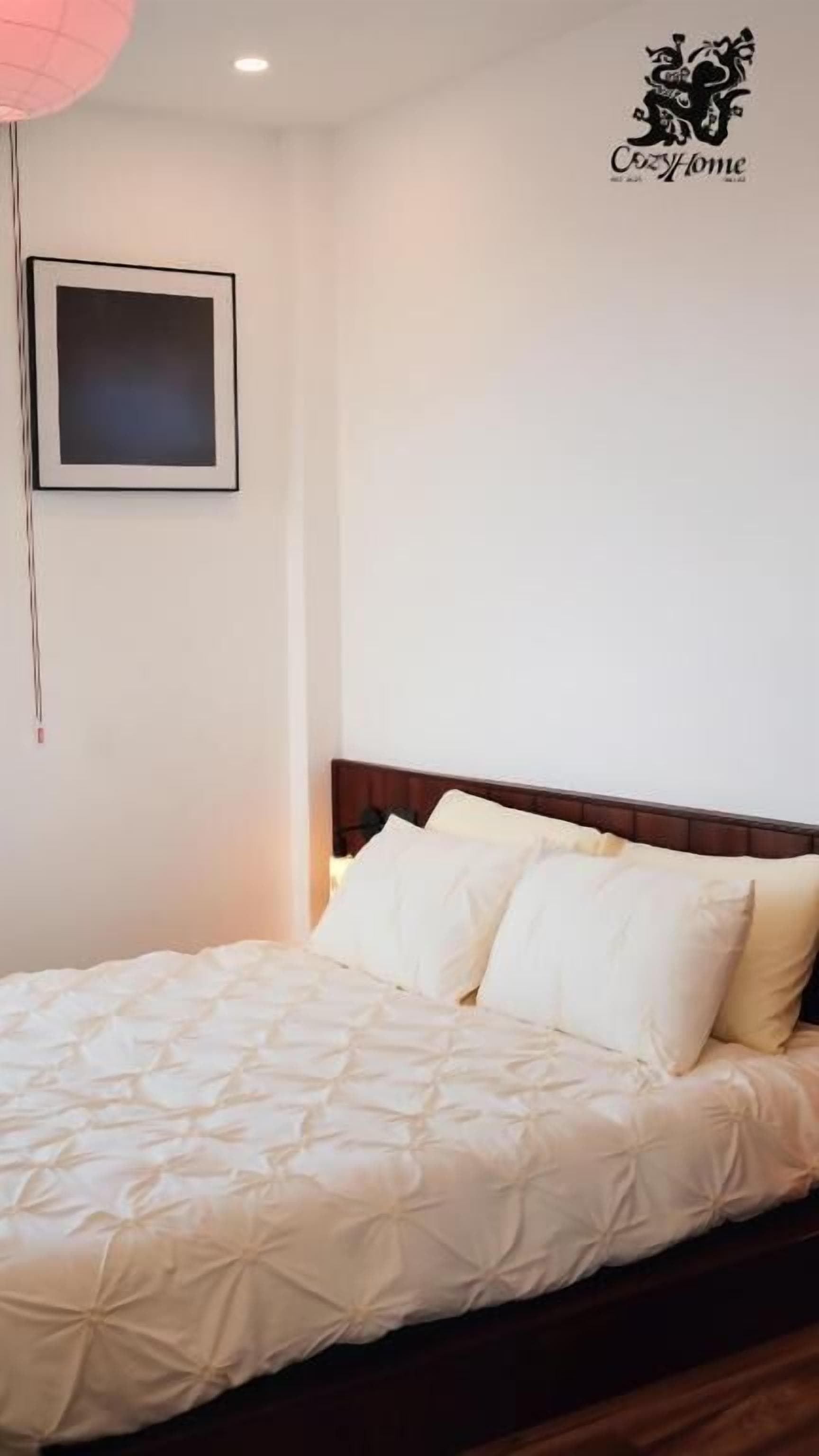 A neatly made bed with a white duvet and pillows, a framed picture on the wall, and a logo in the top right corner.