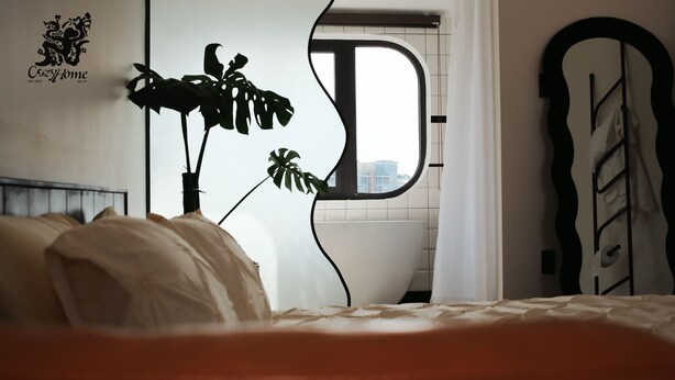 Une chambre à coucher avec un lit, une plante en pot, une fenêtre et un miroir fixé au mur.