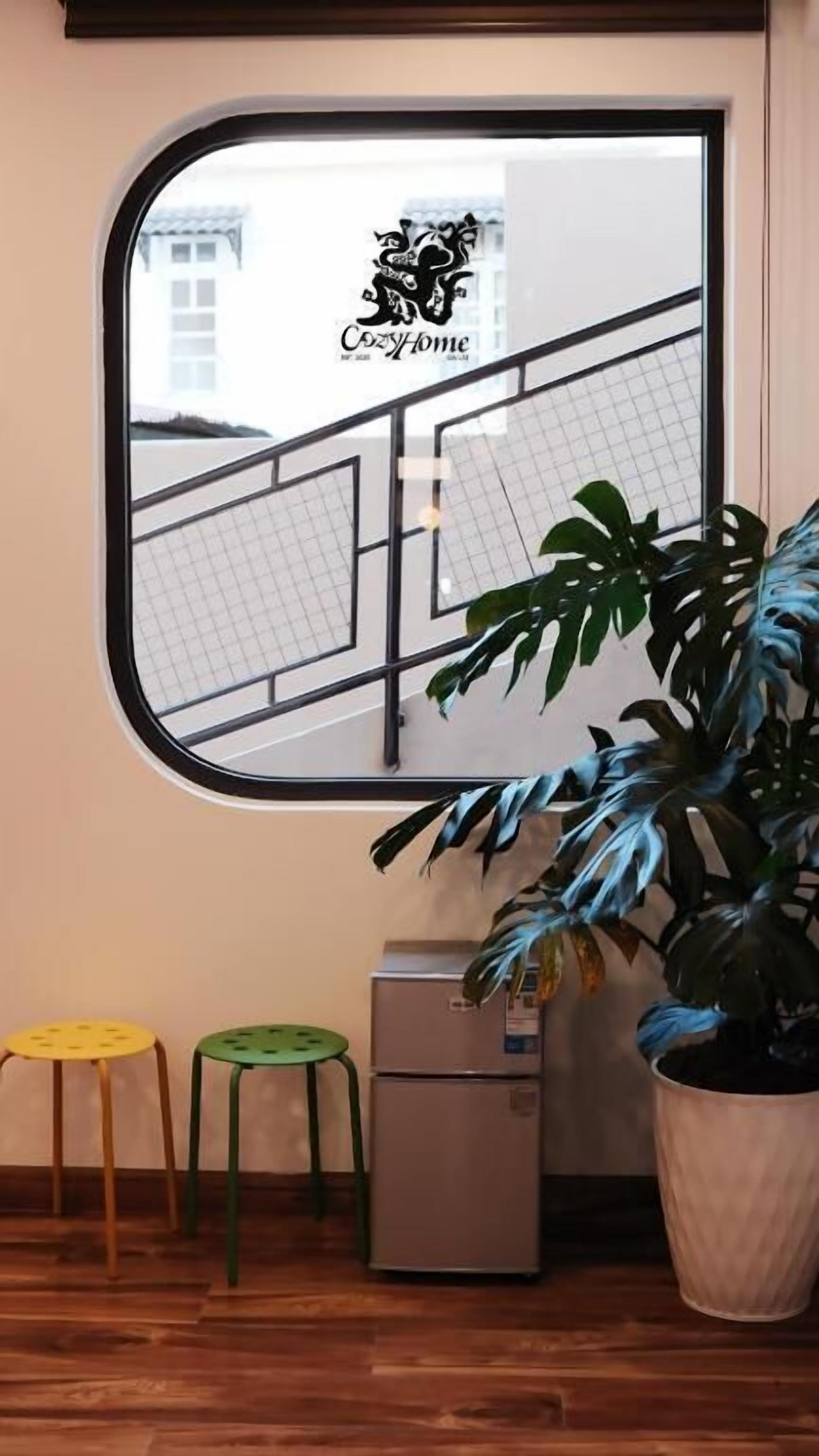 A room with a large window, a potted plant, a small desk, and two stools.