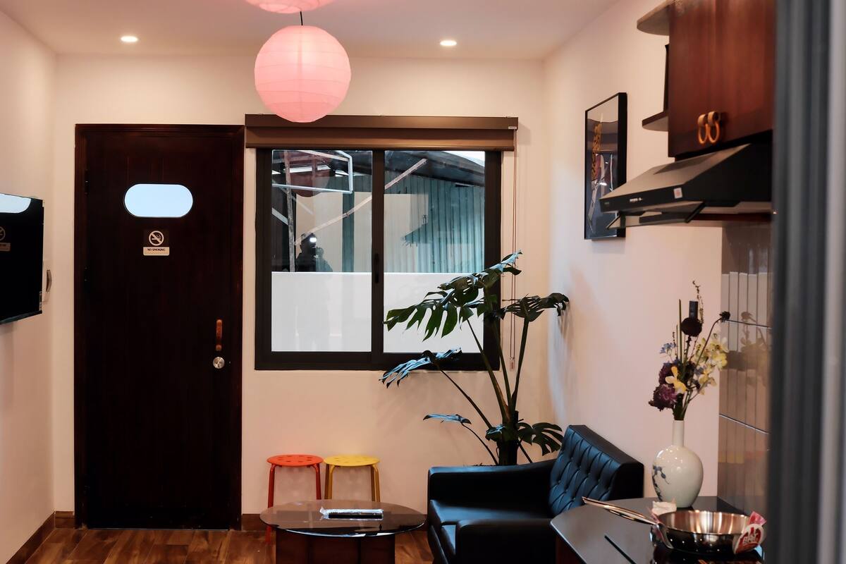 Hall d'hotel con una porta in legno scuro, un cartello ‘No Smoking’, una grande finestra, un divano in pelle nera, un tavolino rotondo e una pianta in vaso.