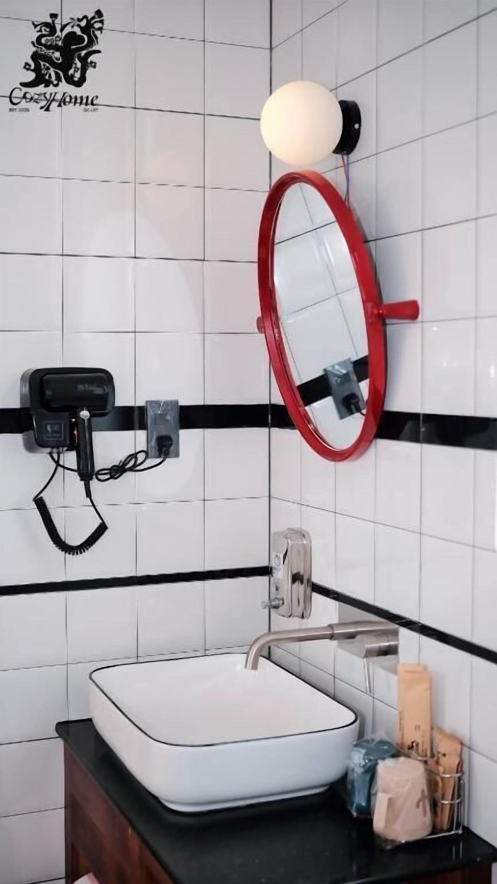 A bathroom with a white sink, a red-framed mirror, a black towel rack, and a white light fixture.
