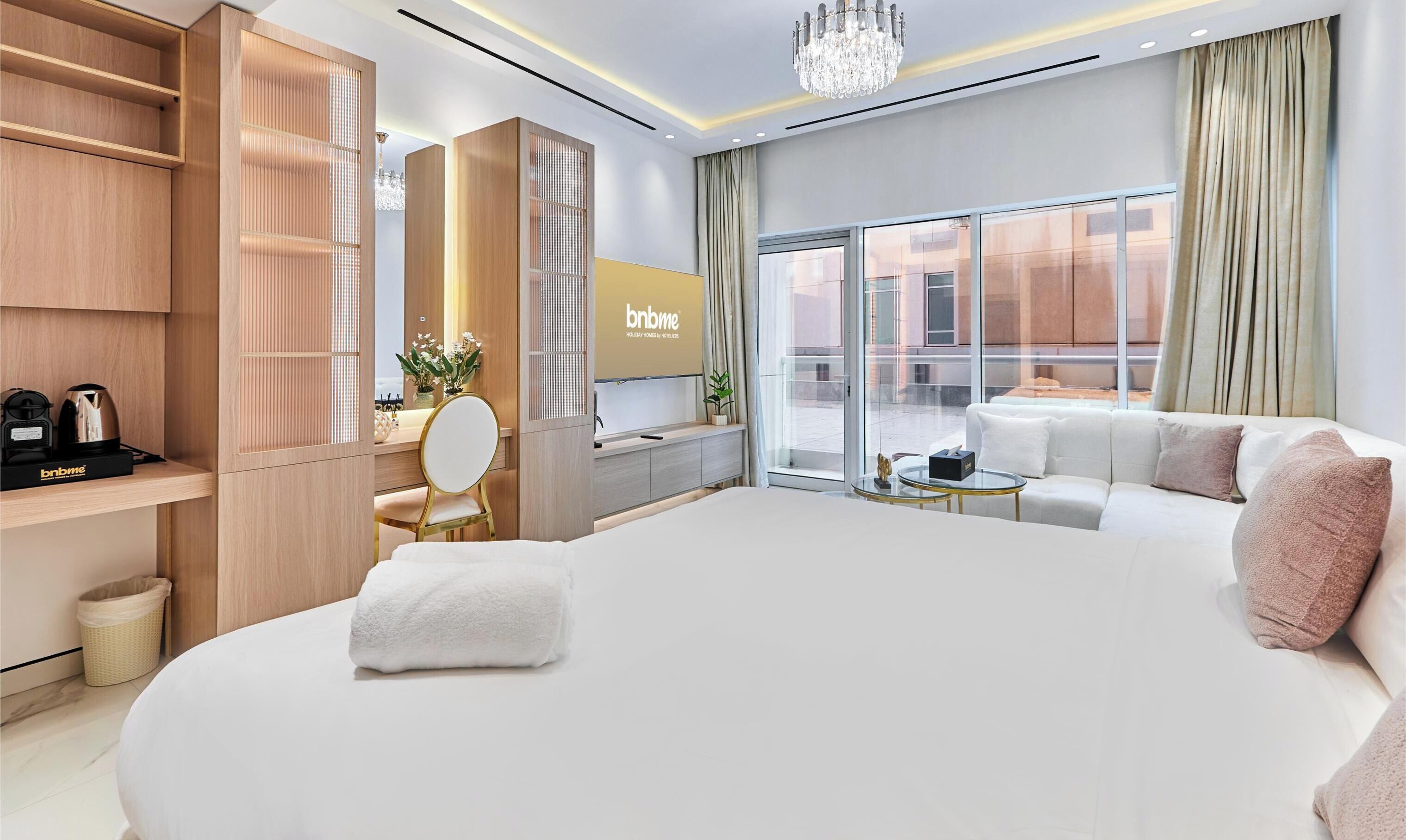 Une chambre d’hôtel moderne avec un grand lit, un bureau doté d’un miroir, une petite table ronde et une vue sur la ville grâce à de grandes fenêtres.