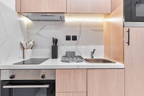 A modern kitchen with a built-in oven, a microwave, a sink, and a range hood. - bnbme - Burj Al Nujoom - Studio (Dubai)