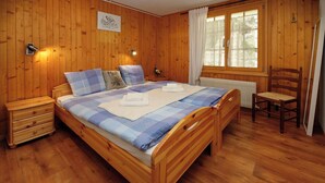 Een slaapkamer met houten lambrisering, een bed, nachtkastje, stoel en raam met gordijnen.